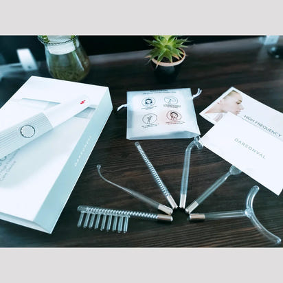 Unboxing photo of the complete Darsonval high-frequency facial machine kit, showing the handle, storage pouch, instructions, and all six electrode tubes on a wooden desk
